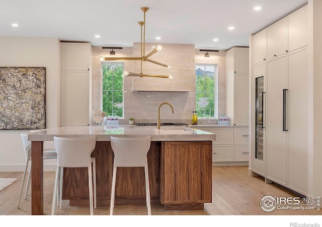 kitchen with light wood-style flooring, white cabinets, light stone countertops, an island with sink, and recessed lighting