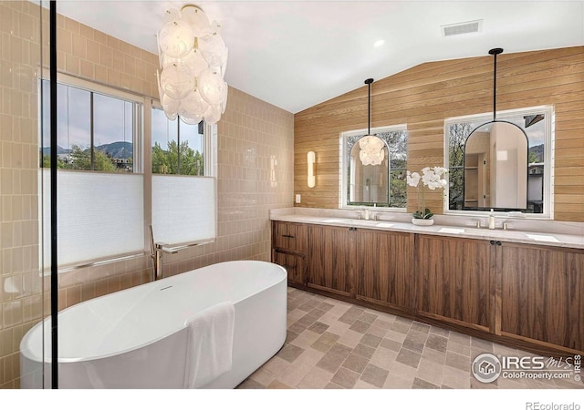 bathroom with lofted ceiling, a freestanding tub, double vanity, tile walls, and wooden walls