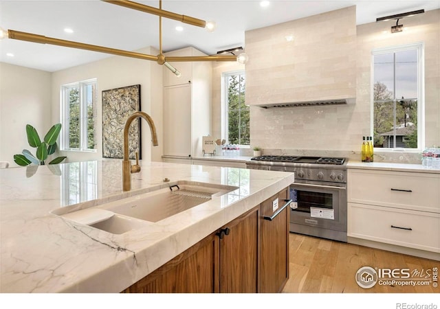 kitchen with high end stainless steel range oven, a sink, tasteful backsplash, light stone counters, and light wood-type flooring