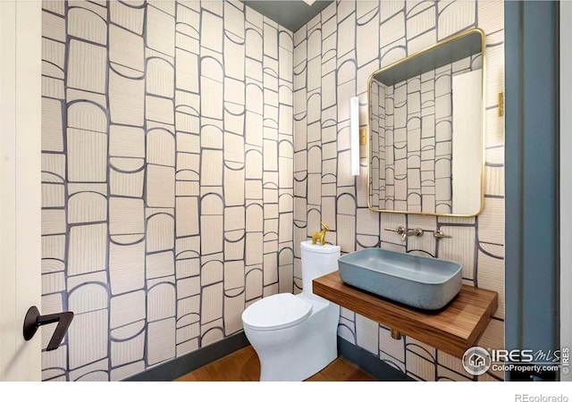 bathroom with wallpapered walls, a sink, toilet, and wood finished floors