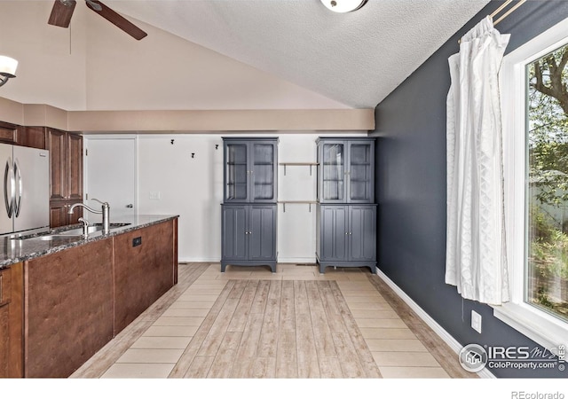 kitchen featuring stainless steel refrigerator, a sink, vaulted ceiling, dark stone countertops, and ceiling fan