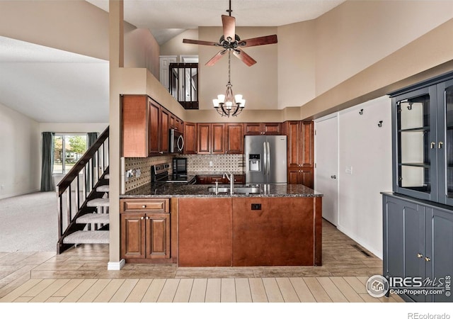 kitchen with appliances with stainless steel finishes, a sink, a ceiling fan, a peninsula, and dark stone countertops