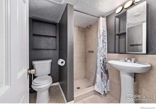 full bathroom featuring tile patterned flooring, toilet, a tile shower, a textured ceiling, and a sink