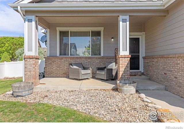 view of exterior entry featuring brick siding, a porch, and fence