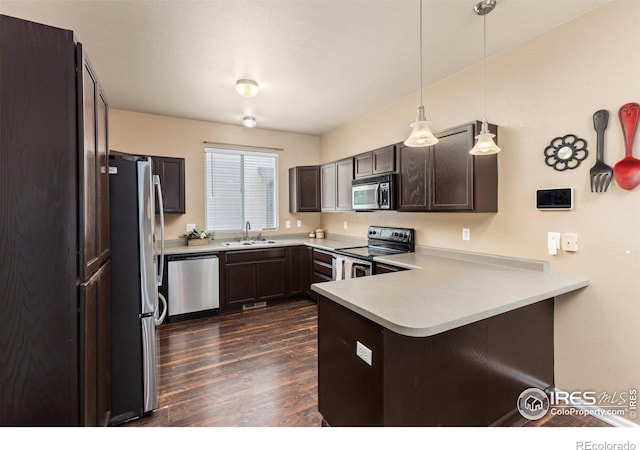 kitchen featuring stainless steel appliances, a sink, a peninsula, dark wood finished floors, and dark brown cabinets