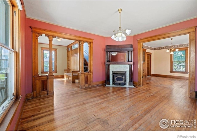 unfurnished living room featuring a chandelier, wood-type flooring, ornamental molding, baseboards, and stairway