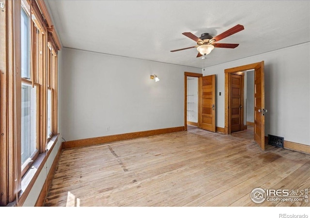 empty room featuring healthy amount of natural light, light wood finished floors, ceiling fan, and baseboards