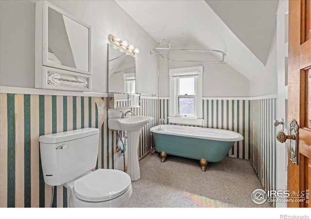 full bathroom featuring a wainscoted wall, toilet, a freestanding bath, lofted ceiling, and wallpapered walls
