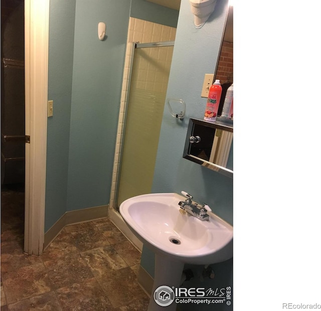 bathroom featuring a sink, stone finish flooring, a shower stall, and baseboards