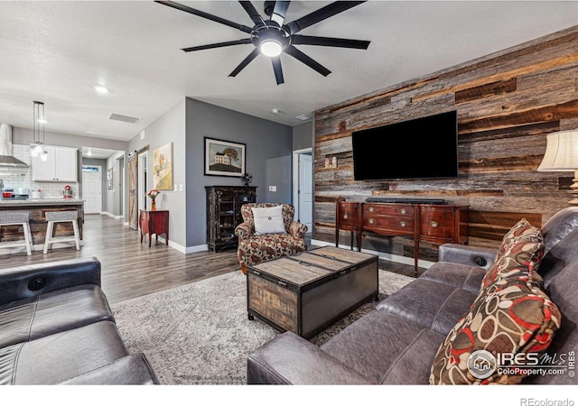 living area featuring a ceiling fan, wood finished floors, baseboards, and wood walls