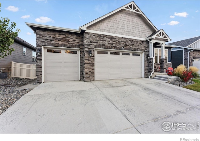 craftsman-style home featuring an attached garage, stone siding, driveway, and fence