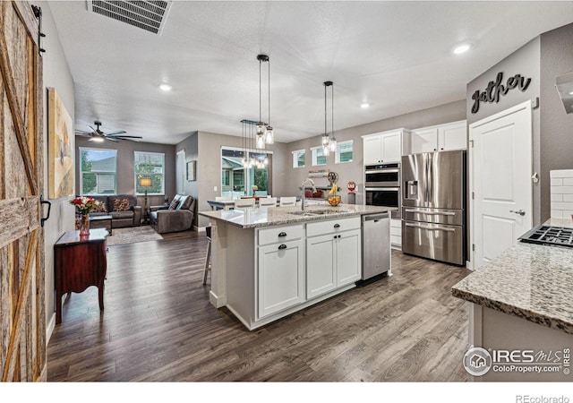 kitchen featuring appliances with stainless steel finishes, a sink, dark wood finished floors, open floor plan, and white cabinets