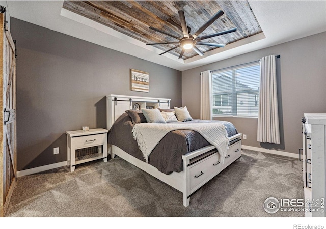 bedroom with a raised ceiling, a barn door, dark colored carpet, baseboards, and wood ceiling