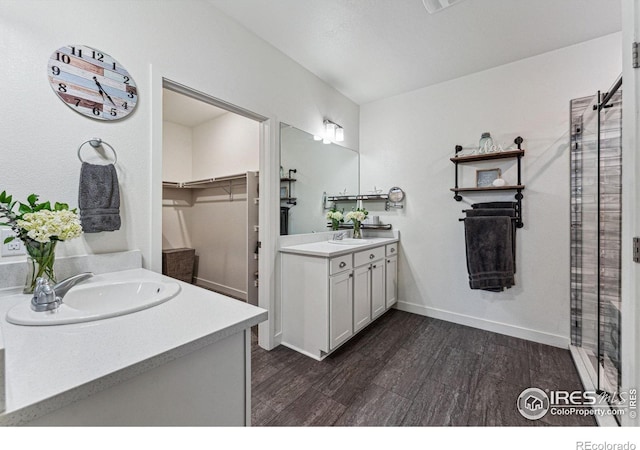 full bath featuring wood finished floors, two vanities, tiled shower, and a walk in closet