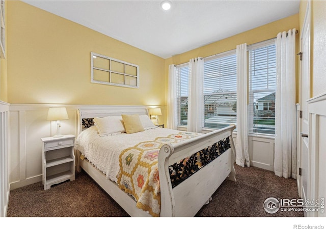 bedroom with dark carpet, a decorative wall, and a wainscoted wall