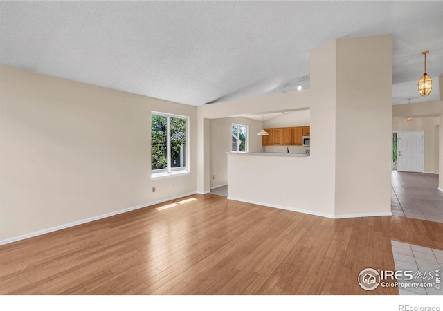 1606 Iris St, Broomfield, CO 80020 - unfurnished living room featuring light wood-style flooring, baseboards, vaulted ceiling, and a textured ceiling