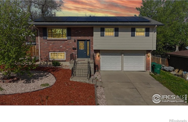 8351 Ralph Ln, Denver, CO 80221 - split foyer home featuring solar panels, a garage, concrete driveway, brick siding, and fence