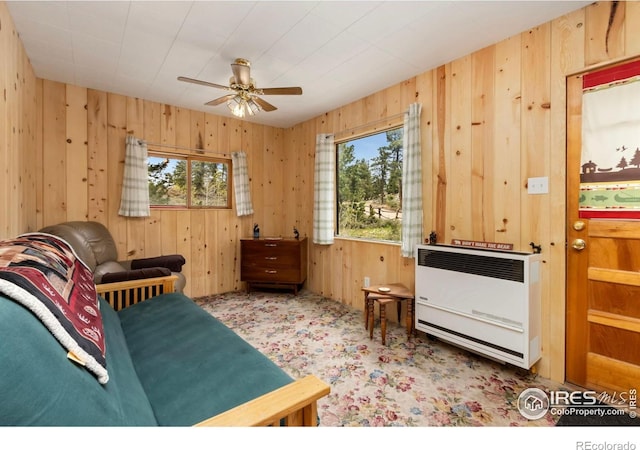 sitting room featuring heating unit, a ceiling fan, wood walls, and carpet floors