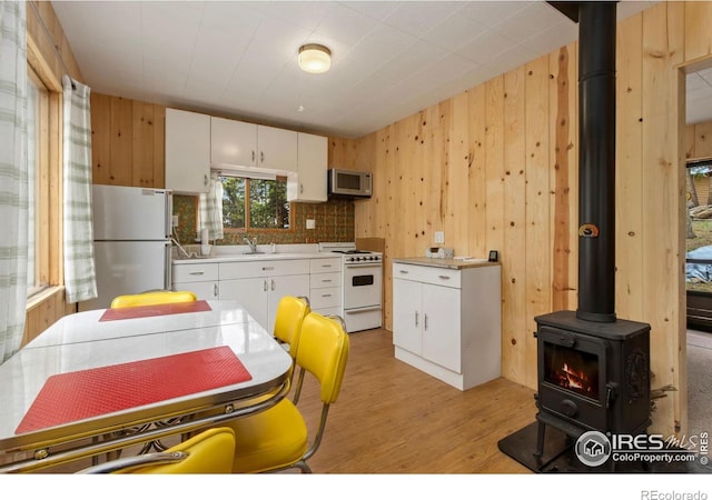 kitchen featuring white appliances, a wood stove, a sink, wooden walls, and white cabinets