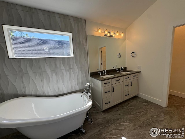full bath featuring marble tiled floors, a freestanding tub, double vanity, lofted ceiling, and baseboards