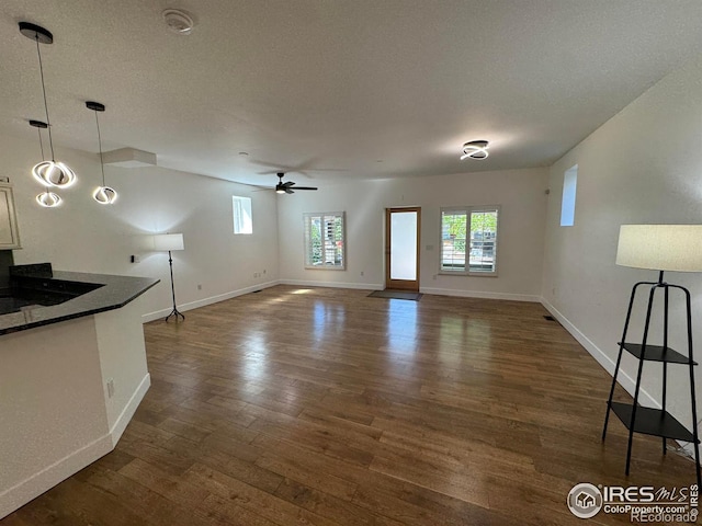 unfurnished living room with dark wood-style flooring, ceiling fan, baseboards, and a textured ceiling
