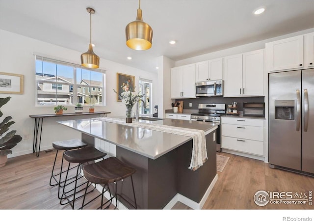 700 Lillibrook Pl, Erie, CO 80026 - kitchen with appliances with stainless steel finishes, a sink, white cabinets, light wood finished floors, and a kitchen breakfast bar
