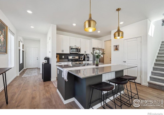 700 Lillibrook Pl, Erie, CO 80026 - kitchen featuring stainless steel appliances, wood finished floors, white cabinetry, a sink, and a kitchen breakfast bar