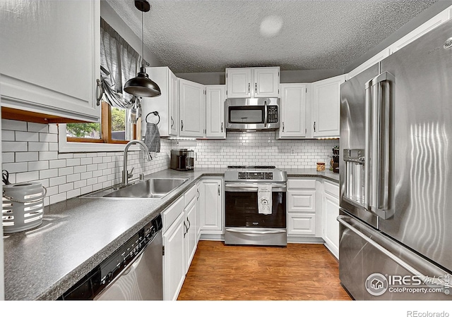 kitchen with appliances with stainless steel finishes, a sink, decorative backsplash, dark countertops, and a textured ceiling