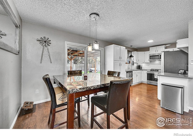 dining room with dark wood finished floors, a textured ceiling, baseboards, and recessed lighting