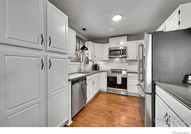 kitchen with stainless steel appliances, a sink, a textured ceiling, tasteful backsplash, and white cabinetry