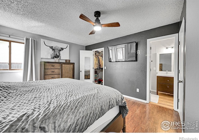 bedroom with a textured ceiling, wood finished floors, a sink, a spacious closet, and a textured wall