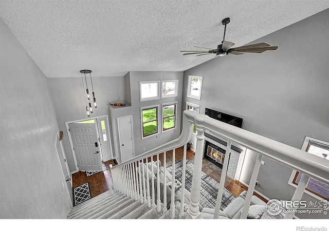 foyer entrance featuring a ceiling fan, wood finished floors, lofted ceiling, a fireplace, and a textured ceiling