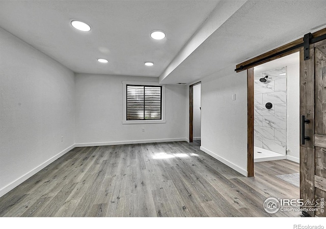 spare room with a barn door, baseboards, wood finished floors, and recessed lighting