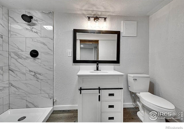 full bathroom featuring wood finished floors, a textured wall, baseboards, toilet, and vanity