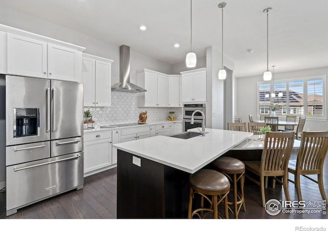 4843 Mariana Hills Cir, Loveland, CO 80537 - kitchen featuring stainless steel appliances, wall chimney range hood, dark wood-style floors, decorative backsplash, and a breakfast bar area