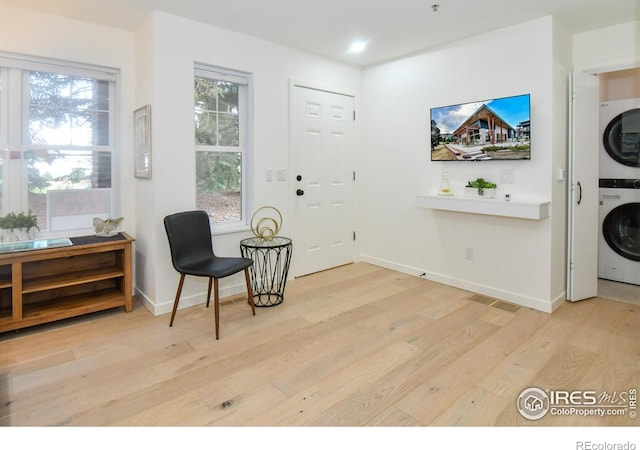 living area with stacked washer / drying machine, light wood-style floors, baseboards, and plenty of natural light