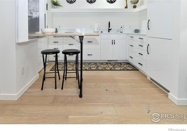 kitchen featuring light wood-style floors, white cabinets, light countertops, a sink, and baseboards