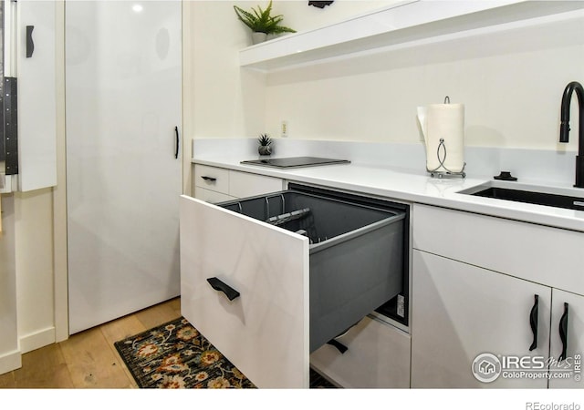 kitchen with white cabinets, light wood-type flooring, a sink, and light countertops