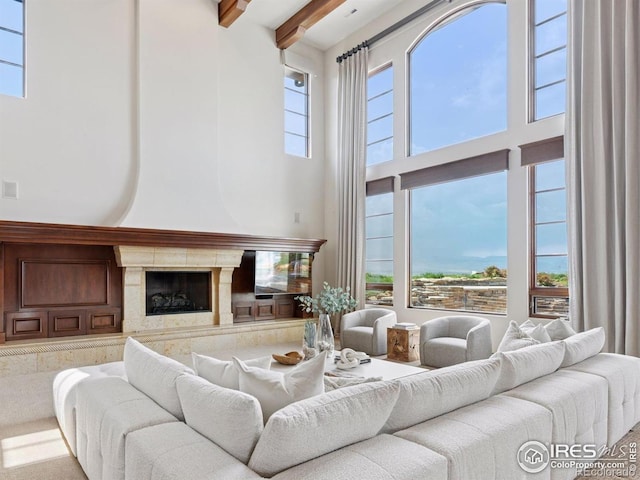 living area featuring a towering ceiling, healthy amount of natural light, beam ceiling, and a high end fireplace