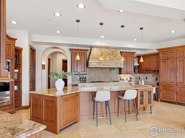 kitchen with open shelves, wall chimney exhaust hood, recessed lighting, tasteful backsplash, and brown cabinetry