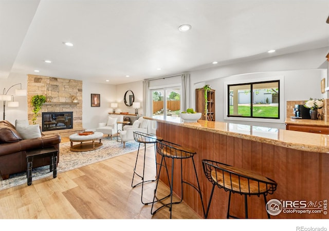 2017 Vaquero St, Longmont, CO 80504 - kitchen with light wood finished floors, recessed lighting, light stone counters, a stone fireplace, and a kitchen bar