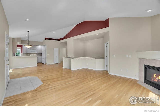 3742 Florentine Cir, Longmont, CO 80503 - unfurnished living room featuring light wood-type flooring, lofted ceiling, a tiled fireplace, baseboards, and recessed lighting