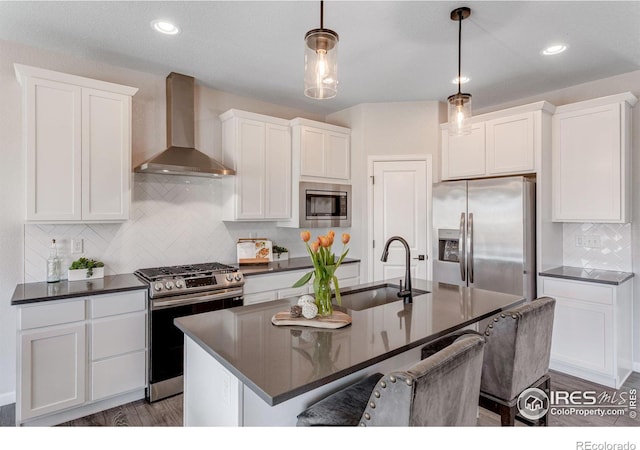 kitchen with wall chimney exhaust hood, stainless steel appliances, a sink, dark countertops, and recessed lighting
