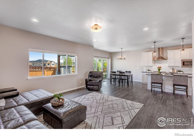 living room featuring recessed lighting, dark wood finished floors, a textured ceiling, a chandelier, and baseboards