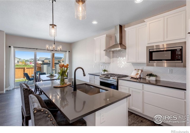 kitchen featuring wall chimney exhaust hood, a sink, appliances with stainless steel finishes, dark countertops, and recessed lighting