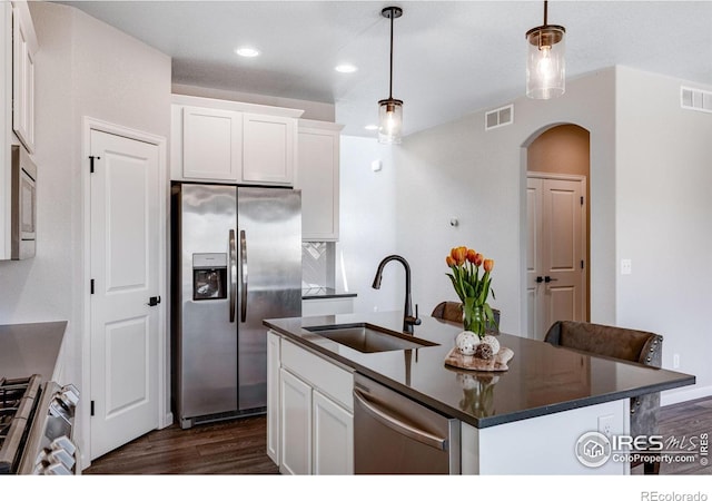 kitchen featuring stainless steel appliances, a sink, arched walkways, dark countertops, and dark wood-style floors