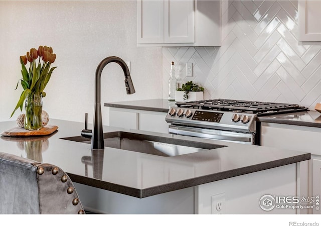 kitchen view of dark countertops, gas stove, backsplash, and white cabinets