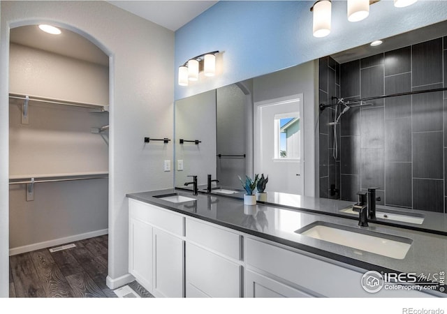 bathroom with wood finished floors, double vanity, a tile shower, and a spacious closet