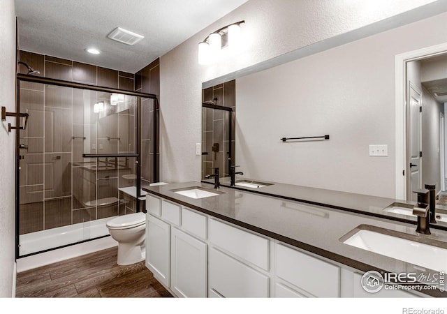 full bath with toilet, a shower stall, wood finished floors, double vanity, and a textured ceiling