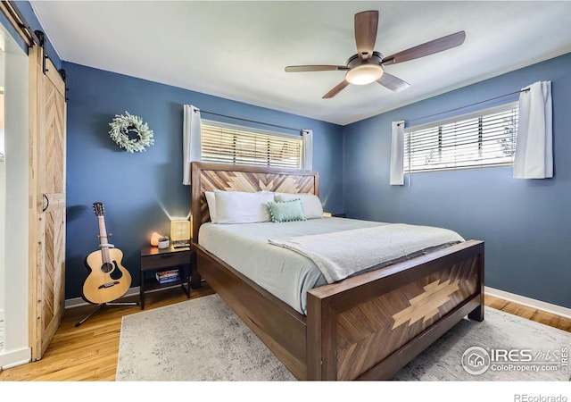 bedroom with a barn door, light wood-type flooring, baseboards, and a ceiling fan